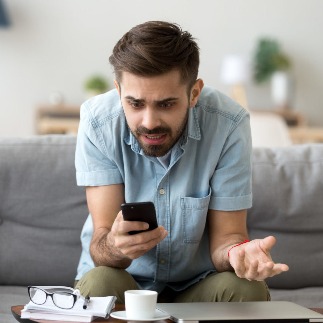 Confused man using phone sitting on couch