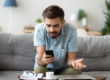 Confused man using phone sitting on couch