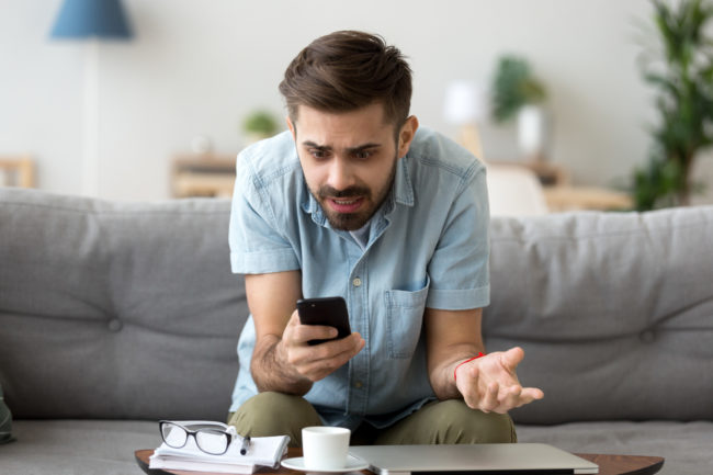 Confused man using phone sitting on couch
